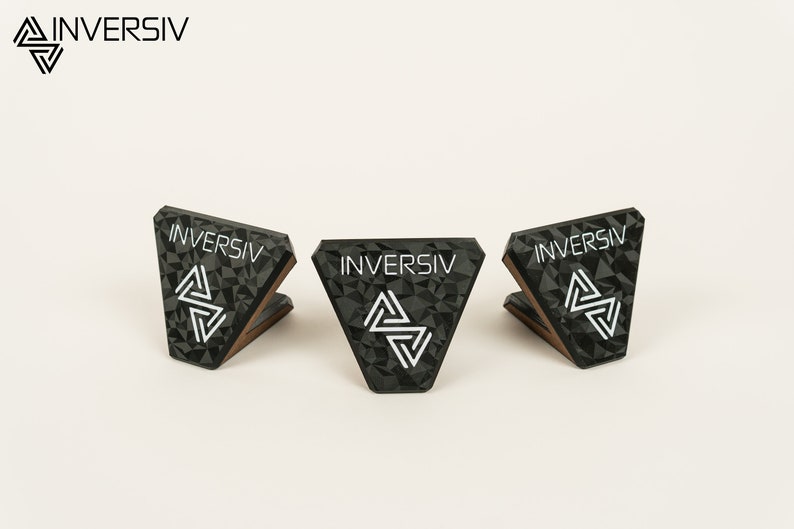 May include: Three black triangular stands with a geometric pattern and the word "INVERSIV" printed in white. The stands are made of a textured material and have a wooden base.