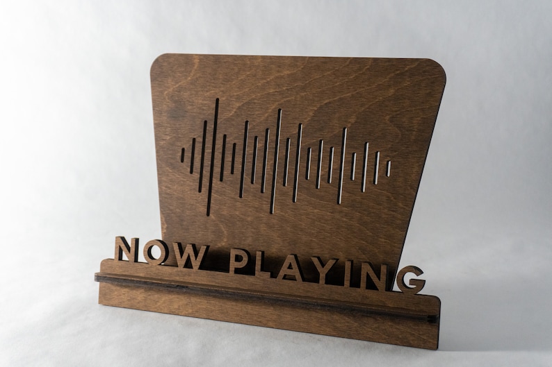 Pode incluir: Uma placa de madeira com as palavras "NOW PLAYING" e um gr&aacute;fico de onda sonora. A placa &eacute; marrom e tem um visual r&uacute;stico.