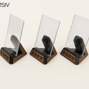 May include: Three wooden display stands with clear acrylic inserts. Each stand features a triangular base with a black top and a brown wood bottom. The base is engraved with the word "INVERSIV" and a symbol.