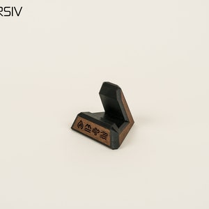 May include: A black and brown wooden phone stand with a geometric design and the symbols for fire, earth, air, and water.