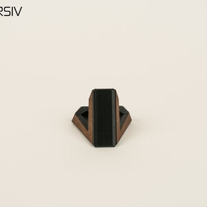 May include: A wooden phone stand with a black accent. The stand is shaped like a triangle and has a small platform on top for holding a phone.