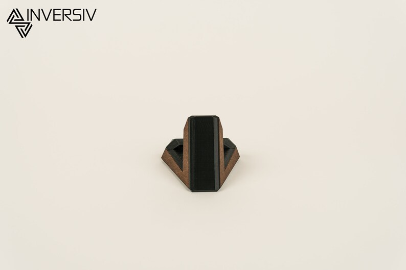 May include: A wooden phone stand with a black accent. The stand is shaped like a triangle and has a small platform on top for holding a phone.