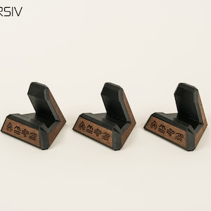 May include: Three black and brown wooden phone stands with a geometric design. Each stand has the symbols for fire, earth, air, and water engraved on the bottom.