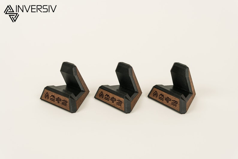May include: Three black and brown wooden phone stands with a geometric design. Each stand has the symbols for fire, earth, air, and water engraved on the bottom.