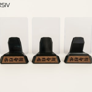 May include: Three black acrylic card display stands with clear acrylic panels. Each stand has a wooden base with a laser-engraved design of four elements: fire, earth, air, and water.