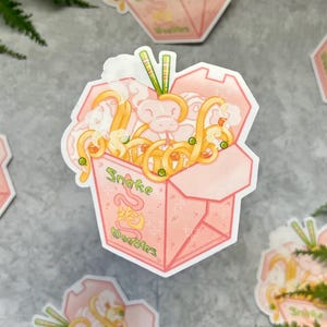 May include: A sticker sheet featuring several stickers of pink takeout boxes filled with noodles. The boxes have the words "Snake Noodles" printed on them. The noodles are yellow and the snake is pink.