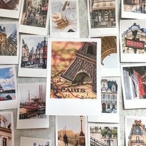 May include: A collection of Polaroid-style photos featuring various Parisian landmarks, including the Eiffel Tower, street scenes, and a map of Paris. The photos are arranged on a white surface.