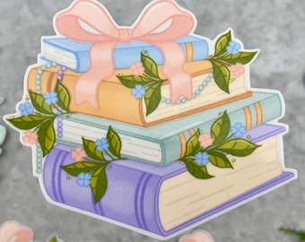 May include: A sticker featuring a stack of four books in shades of blue, yellow, teal, and purple. A light pink ribbon is tied around the top book. The stack is decorated with green leaves, small blue and pink flowers, and a string of white pearls.