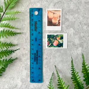 2 Cozy Fall themed polaroid style stickers next to a six inch blue ruler to show they are Width: 1.40 inches by Height: 1.75 inches. Pictures and ruler are on a light gray background with green fern leaves.
