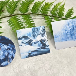 May include: Three winter-themed images featuring snowy landscapes. The first image is a close-up of a blue spruce tree branch. The second image shows a waterfall cascading through a snowy forest. The third image shows a snowy forest with tall trees.