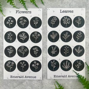 May include: Two white cards with black circles featuring floral and leaf illustrations. The card on the left says "Flowers" and the card on the right says "Leaves". The text "Emerald Avenue" is at the bottom of each card. Ferns are in the background.