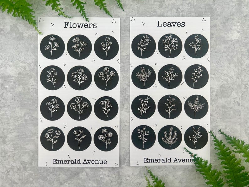 May include: Two white cards with black circles featuring floral and leaf illustrations. The card on the left says "Flowers" and the card on the right says "Leaves". The text "Emerald Avenue" is at the bottom of each card. Ferns are in the background.