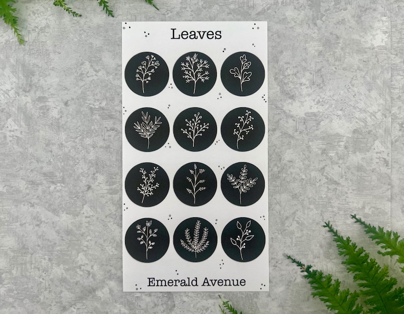 May include: A sheet of stickers with the word "Leaves" at the top and "Emerald Avenue" at the bottom. Each sticker is a black circle with a white botanical illustration. The stickers feature various leaf and plant designs.