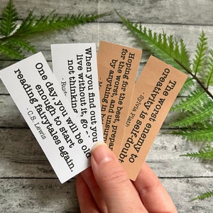 Book quotes by Sylvia Plath, C.S. Lewis, and others in brown and white sticker paper strips being held by hand to show scale.