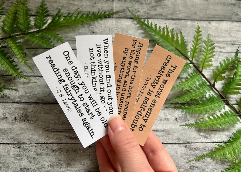 Book quotes by Sylvia Plath, C.S. Lewis, and others in brown and white sticker paper strips being held by hand to show scale.