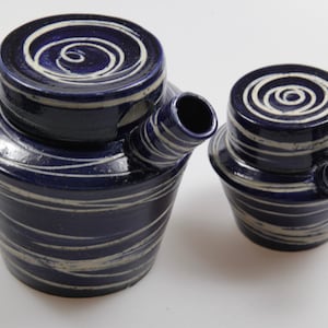 Könnte beinhalten: Zwei blaue und weiße Keramik-Teekannen mit einem wirbelnden Muster. Die größere Teekanne hat einen Ausguss und einen Deckel. Die kleinere Teekanne hat einen Ausguss, aber keinen Deckel.