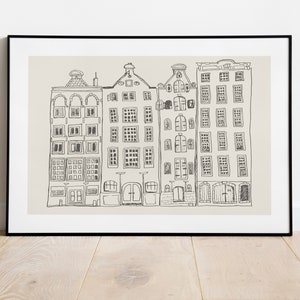 May include: A framed wall art print featuring a black line drawing of four narrow, multi-storey canal houses with varied gabled roofs and numerous rectangular windows, set against a solid light beige background within a thin black frame.