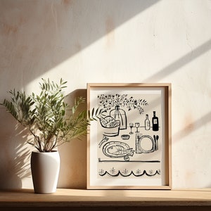 May include: A framed black and white line art print depicting a dining table scene with a fish on a plate, a bowl of bread, glasses, and a vase of flowers. The artwork is displayed in a light wood frame next to a green plant in a white pot.