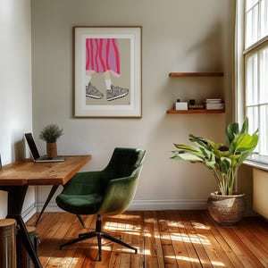 May include: A green office chair with a wooden desk and a framed illustration of a person wearing a pink and white striped skirt and grey sneakers. A potted plant is in the corner of the room.