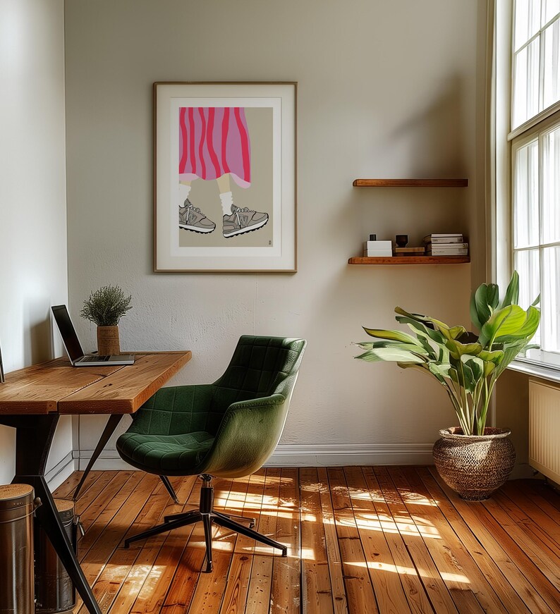 May include: A green office chair with a wooden desk and a framed illustration of a person wearing a pink and white striped skirt and grey sneakers. A potted plant is in the corner of the room.