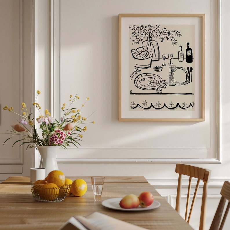 May include: A framed wall art print featuring a black line drawing on a beige background. The illustration depicts a dining table setting with a fish on a platter, a vase of flowers, wine bottles, glasses, and a bowl of bread, all framed in light wood.