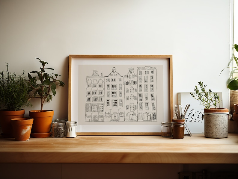 May include: A framed line art print featuring a row of four tall, narrow buildings with detailed windows and gabled roofs. The drawing is rendered in dark grey lines on a light beige background, enclosed in a simple, light-toned wooden frame.