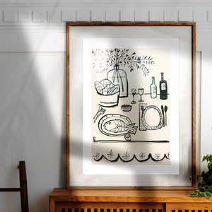 May include: A framed wall art print featuring a black line drawing on a cream background. The illustration depicts a dining table set with a fish on a plate, a bowl of bread, wine glasses, bottles, and cutlery. The bottom border has a scalloped pattern.