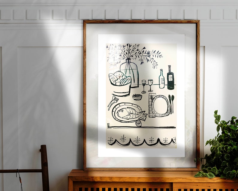 May include: A framed wall art print featuring a black line drawing on a cream background. The illustration depicts a dining table set with a fish on a plate, a bowl of bread, wine glasses, bottles, and cutlery. The bottom border has a scalloped pattern.