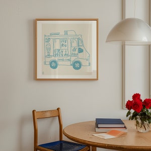 May include: A framed illustration of a blue ice cream truck with the words "Shakes, Cones" on the side. The truck is filled with ice cream cones and cups. The frame is light brown wood.