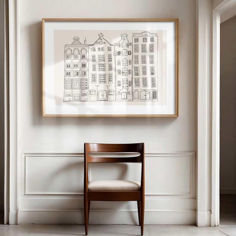 May include: A framed wall art print featuring a black line drawing of four narrow, multi-story buildings with varied roof shapes on a light beige background. The artwork is enclosed in a simple, light-toned wooden frame and hangs on a white wall.