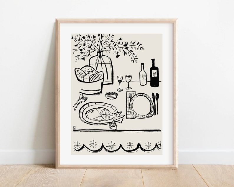May include: A framed line art print featuring a black ink illustration on a light beige background. The drawing depicts a dining table set with a fish on a platter, a bowl of bread, two wine glasses, two bottles, cutlery, and a vase of flowers.