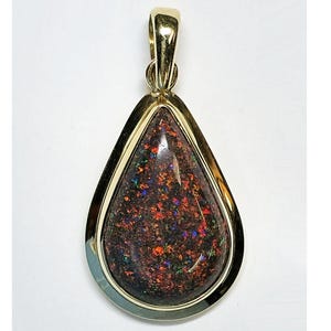 May include: A gold-framed pendant in a teardrop shape, featuring a dark, speckled stone with red, orange, blue, and green flecks. The pendant has a polished gold bezel and a gold bail for a chain.