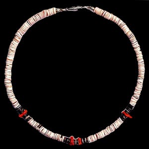 May include: A white shell necklace with red coral accents. The necklace is made of small, round shells that are strung together on a cord. The coral accents are small and are spaced evenly throughout the necklace.