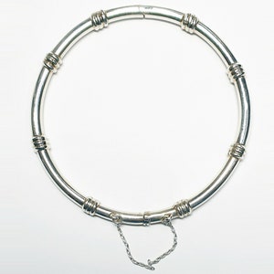 Peut inclure: Un bracelet jonc en argent avec une fermeture à charnière et des accents décoratifs. Le bracelet est fait d'un métal lisse et poli et a un design simple et élégant.