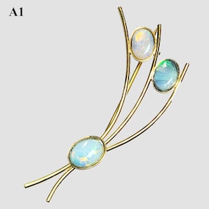 May include: A gold-toned brooch featuring three oval opals. The opals are set within a delicate, flowing design. The brooch has a pin closure on the back. The text "A1" is in the upper left corner.