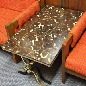 May include: A square-shaped side table with a brown and white marbled top and a gold and black metal base. The table is sitting between two orange chairs.