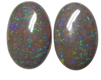 May include: Two oval-shaped black opals with iridescent green, blue, and red flashes. The opals are set in a cabochon cut.