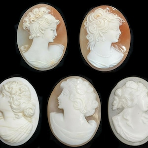 Pode incluir: Cinco pingentes de camafeu com esculturas detalhadas de perfis de mulheres. Os camafeos são feitos de concha branca e estão engastados em molduras ovais. As molduras são feitas de diferentes materiais, incluindo marrom, cinza e branco.