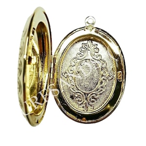 Pode incluir: Um medalhão oval dourado com uma tampa articulada. O medalhão tem um design decorativo na frente e está aberto para revelar o interior vazio.