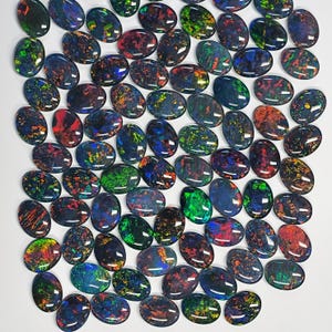 May include: A collection of oval-shaped opals with a polished, glossy finish. The opals display a variety of colors, including green, blue, red, and yellow, with a dark base color. The gemstones are arranged closely together, showcasing their unique patterns.