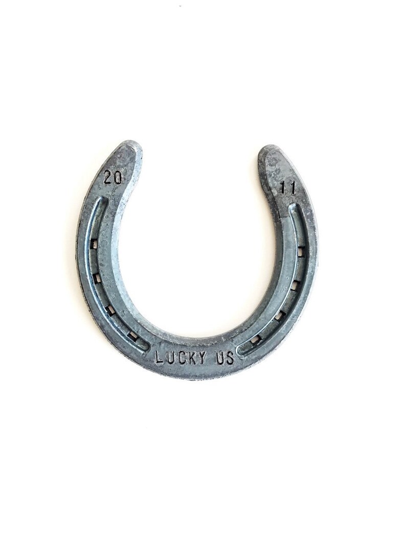 May include: A silver horseshoe with the numbers "20" and "11" stamped on each side. The horseshoe has the words "LUCKY US" stamped on the bottom.