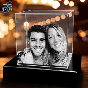May include: A 3D crystal cube with a black base, featuring a black and white engraved image of a couple smiling at the camera.