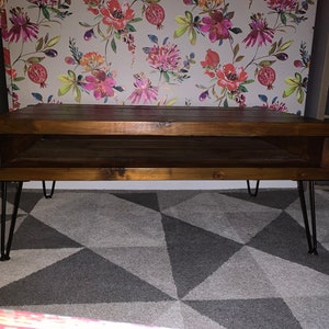 May include: A dark brown wooden coffee table with a lower shelf and hairpin legs. The table is sitting on a gray and white geometric patterned rug.