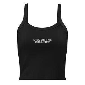 Op de afbeelding: Een zwarte mouwloze crop top met een ronde halslijn en brede schouderbanden. In het midden van de borst staat de witte tekst DIBS ON THE DRUMMER gedrukt in een strak, schreefloos lettertype. Het kledingstuk heeft een rechte zoom aan de onderkant.