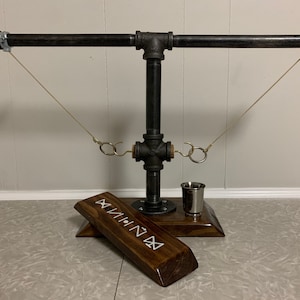 May include: A black metal pipe and wood game with two strings and rings. The game has a small cup and a wooden base with the word "VIIIIIIN" carved into it.
