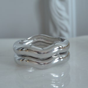 May include: Two silver wavy rings stacked on top of each other. The rings are smooth and shiny.