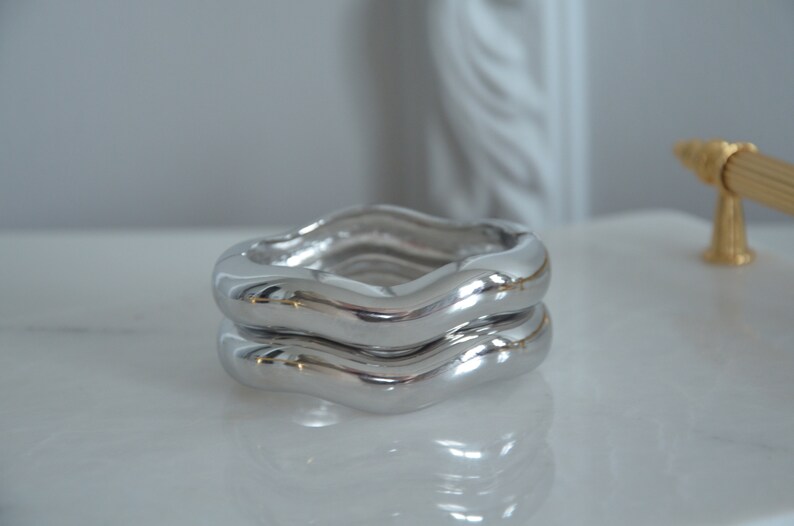 May include: Two silver wavy rings stacked on top of each other. The rings are smooth and shiny.