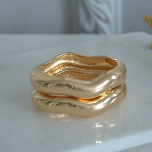May include: Two gold-toned, wavy, open bangle bracelets stacked on top of each other.