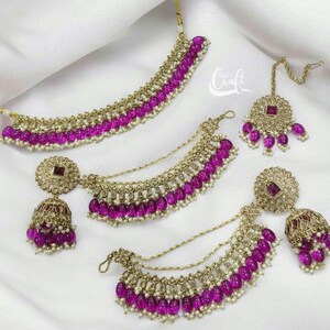 Puede incluir: Un conjunto de joyas doradas con cuentas rosas y piedras transparentes. El conjunto incluye un collar, un par de pendientes y un maang tikka.