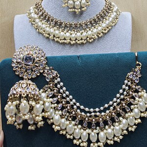 Puede incluir: Un conjunto de collar y pendientes de oro y perlas blancas. El collar tiene varias capas de perlas y cristales. Los pendientes son grandes y tienen forma de l&aacute;grima.